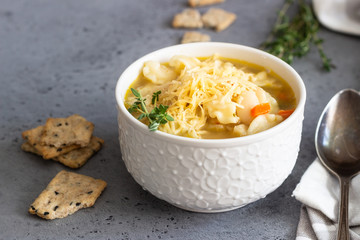Two white bowls of Italian soup minestrone with pasta and white beans topped with fresh thyme and served with crackers on grey concrete background. Vegetarian food concept.