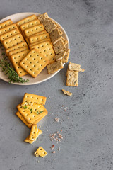 Thin crispy salted crackers with seeds and herbs on grey concrete background. 