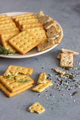 Thin crispy salted crackers with seeds and herbs on grey concrete background. 