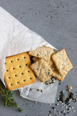 Thin crispy salted crackers with seeds and herbs on grey concrete background. 