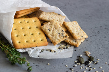 Thin crispy salted crackers with seeds and herbs on grey concrete background. 