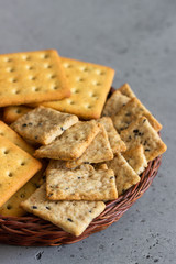 Thin crispy salted crackers with seeds and herbs on grey concrete background. 