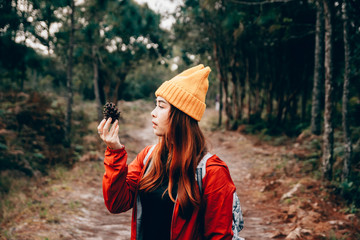 Traveler girl wear yellow knit hat, with backpack in the forest, and looking a pine cone. Warm tone preset.