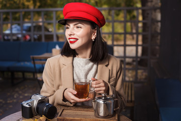 Young beautiful girl in red hat is drinking tea in a cafe. Autumn