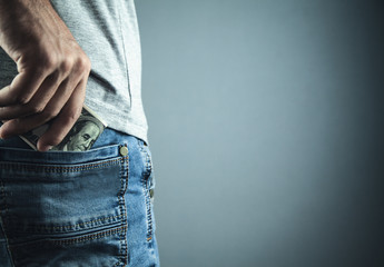 Caucasian man put a dollar in a jeans pocket.