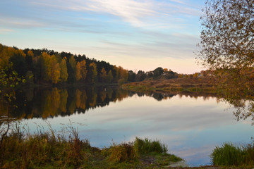 Dawn in the forest near the lake. The forest is reflected in the water. Autumn Early morning. Russia