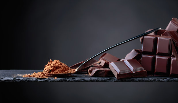 Broken chocolate pieces and cocoa powder on black background.