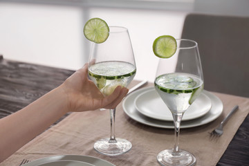 Woman holding glass of fresh cucumber water over table