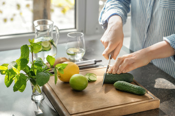 Woman cutting fresh cucumber at table