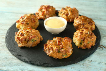 Slate plate with tasty sausage balls and cheese sauce on wooden table