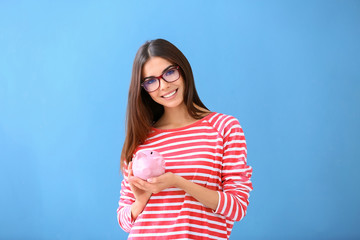Obraz premium Beautiful young woman with piggy bank on color background