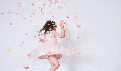 Obraz na płótnie Canvas Cheerful cute little girl wearing pink dress in tulle with princess crown dancing on confetti surprise isolated on white studio wall. Playful toddler girl celebrating her birthday party having fun
