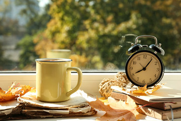 Metal cup of aromatic tea with books and autumn leaves on windowsill