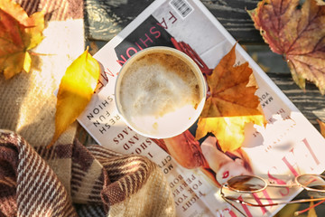 Cup of hot coffee with magazine and autumn leaves on wooden bench