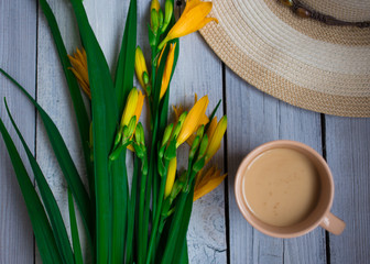 a bouquet of yellow lilies, a hat and a Cup of coffee on a wooden table, breakfast