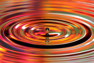 Water drops splash. Red and yellow colored ripples, reflections on water surface