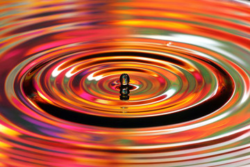 Water drop splashes. Red and yellow colored ripples, reflections on water surface