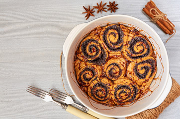 Poppy seed rolls in the baking dish - traditional Hungarian pastry for Thanksgiving and Christmas. Cinnamon buns decorated with winter spices on the gray kitchen background. Top view with copy space