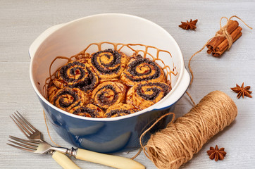 Traditional Hungarian pastry for Thanksgiving and Christmas - poppy seed rolls with chocolate topping in the baking dish decorated with spices. Cinnamon buns on the gray concrete background. Side view
