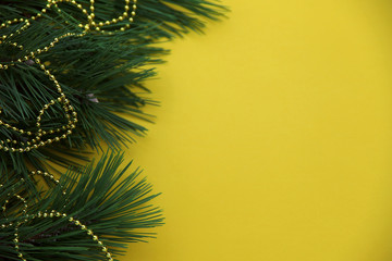Fototapeta na wymiar On a yellow horizontal surface, to the left, lies a pine branch decorated with golden beads. Christmas concept. Cropped shot, close-up, place for text, background.