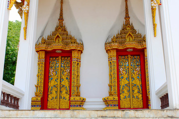 Fototapeta premium Doors and windows of the temple adorned by intricate wooden carvings in golden color depicting Buddha's life familiarized by Jataka Tales, at Ban Bung Sam Phan Nok, Phetchabun, Thailand.