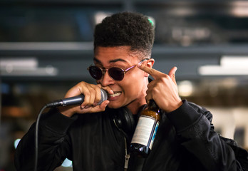 Black rapper performing with microphone, pointing to head with bottle in hand. Headphones around...