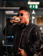 Black rapper performing with microphone, headphones around neck - obrazy, fototapety, plakaty