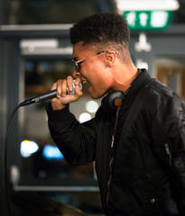 Black rapper performing with microphone. Side profile. Headphones around neck.