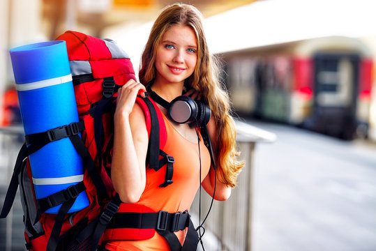 Traveller girl female wear headphones with backpack and tourism outfit at railway station city outdoor. Train locomotive on background.