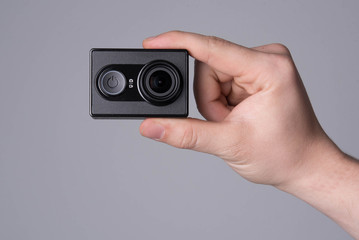 hand holding black action camera on grey background