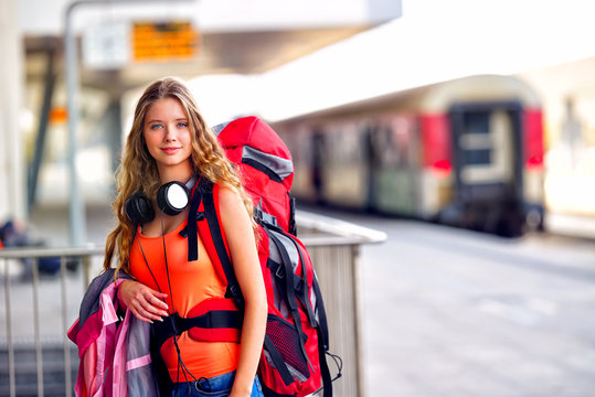 Traveller girl female wear headphones with backpack and tourism outfit at railway station city outdoor. Terminal train locomotive on background.
