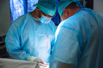 Two doctors in sterile medical clothes perform an operation in a hospital. Professional work in the clinic, surgeons are men with an assistant woman. The concept of health, medicine.
