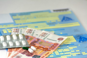 Russia. Close-up, Russian sick leave with seals. The bottle of pills and a few pills in bulk. Russian money-banknotes of 5000 rubles. Focus on the nearest pills.