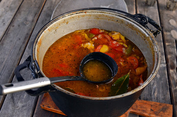Large saucepan with black ladle and gourmet soup with tomatoes and peppers. Cooking, lunch. Delicious recipes. Homemade food. Mistress in the kitchen. Table with food