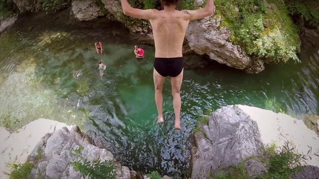 Slow motion of long haired man jumping from rock into river in Soca valley, Slovenia.