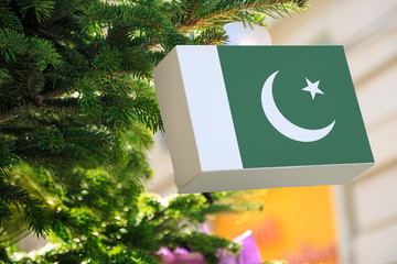 Pakistani flag printed on a Christmas gift box. Printed present box decorations on a Xmas tree branch. Christmas shopping in Pakistan, sale and deals concept.