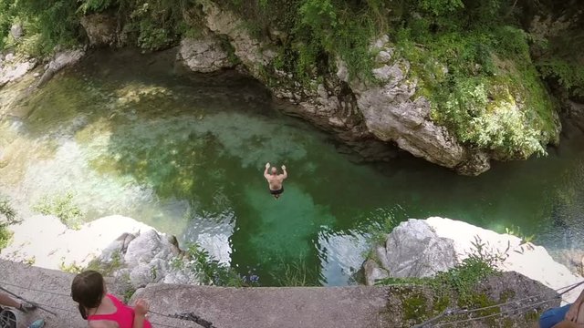 Slow motion of fit man jumping from rock into river in Soca valley, Slovenia.