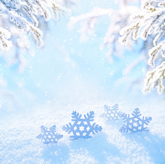 Light Christmas background. Decorative snowflakes close-up in snow on sunny day. Snowy landscape with spruce fir branches covered with snow and falling snow on nature outdoors, copy space