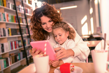 Modern technologies. Charming girl leaning on her mom while staring at her tablet