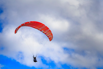 Paraglider with two people (tandem) flying against the blue sky with clouds.