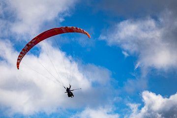Paraglider with two people (tandem) flying against the blue sky with clouds.