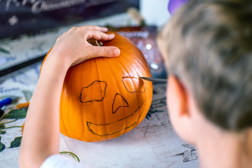 blond boy carving pumpkin jack-o-lantern with knife