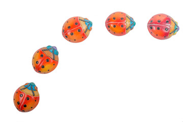 Flat lay of a curved line formed by a group of five ceramic ladybugs on a white studio background, red, orange, yellow, blue and black colors. Space for text