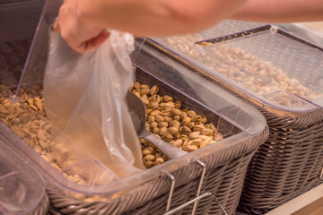 young woman hands taking pistachios into plastic bag at grocery shop