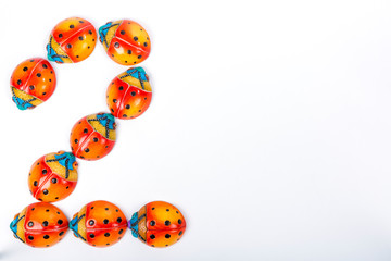Flat lay with the number 2 formed by a group of ceramic ladybugs with red, orange, yellow, blue and black colors on a white background with space for text