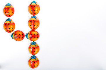 Flat lay with the number 4 formed by a group of ceramic ladybugs with red, orange, yellow, blue and black colors on a white background with space for text