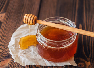 Honey in a jar with a honey dipper on a wooden background