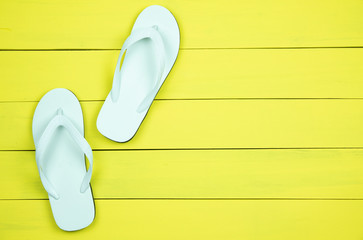 White flip flops on yellow wood background.