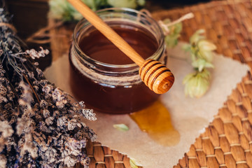 Honey in a jar with a honey dipper on a wooden background with lavender and hop flowers