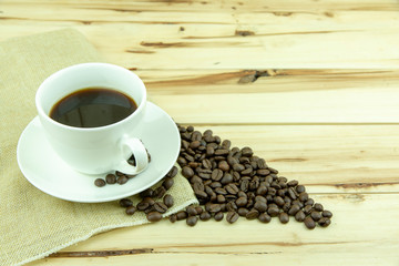 Cup of coffee with coffee beans on wood background.